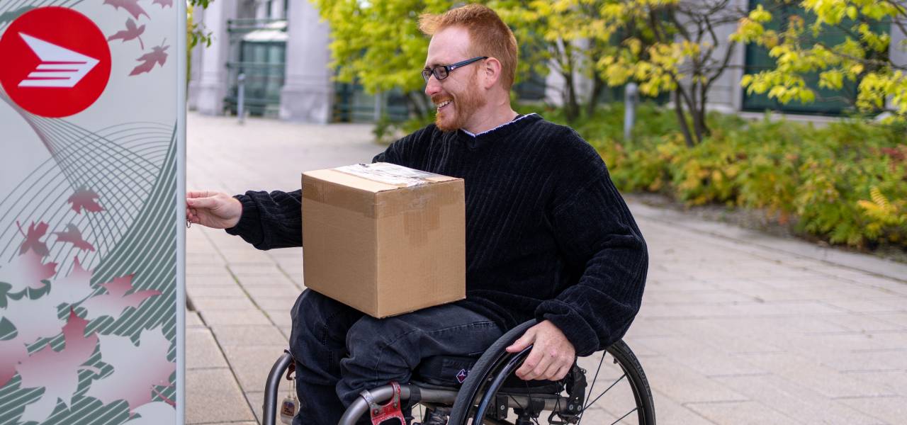 A man in a wheelchair takes a package from a Canada Post community mailbox.