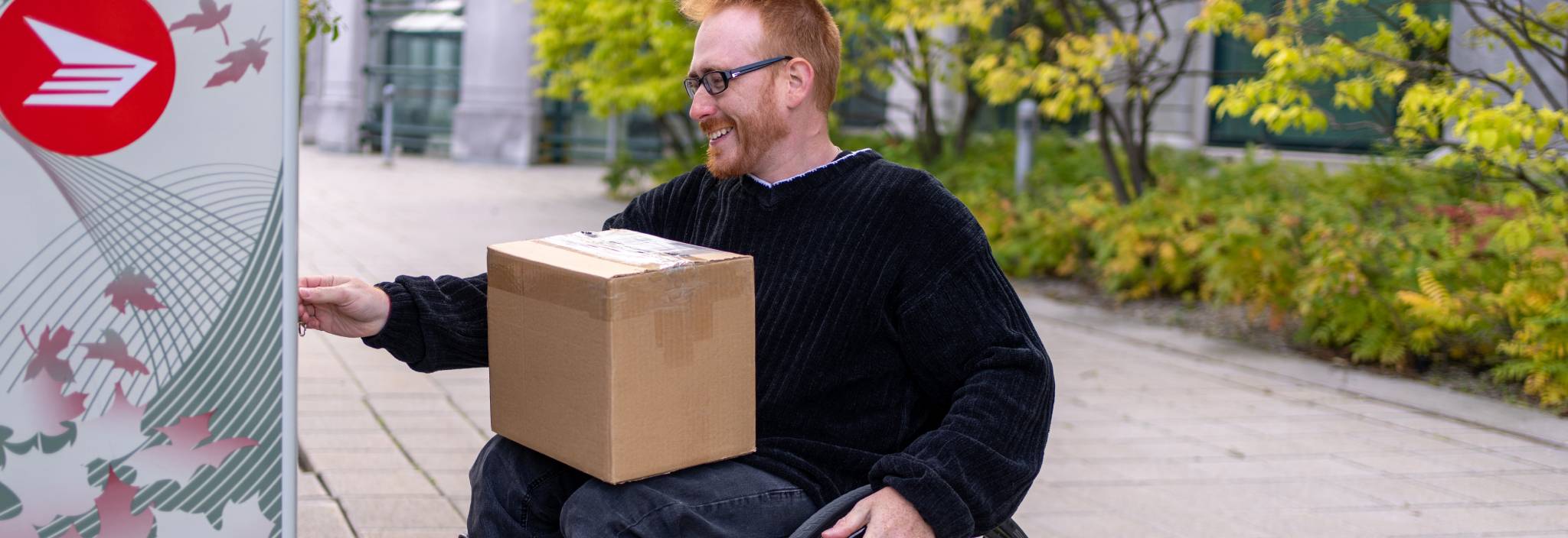 A man in a wheelchair takes a package from a Canada Post community mailbox.