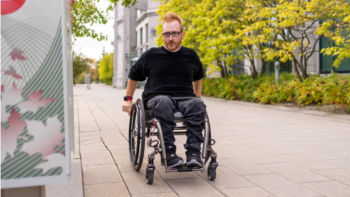 A man in a wheelchair approaches an accessible community mailbox. A man in a wheelchair approaches an accessible community mailbox.