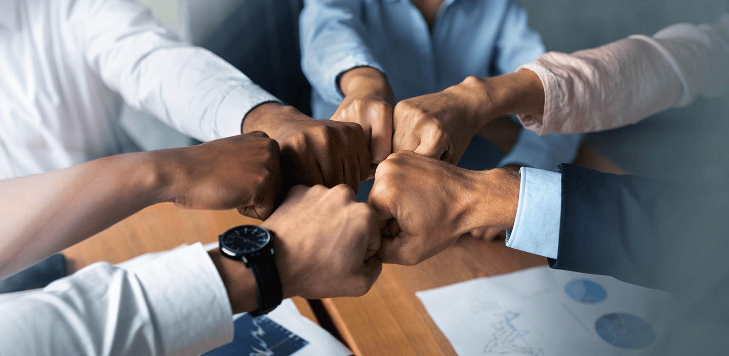 Six people bumping fists in a gesture of unity and teamwork during a business meeting.