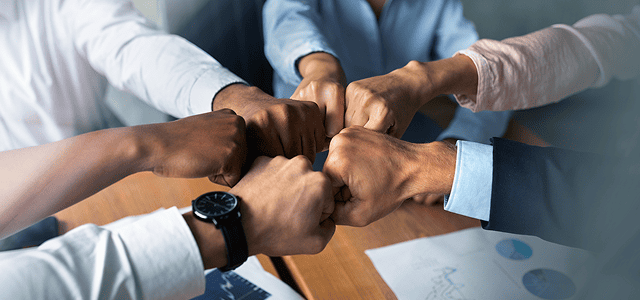 Six people bumping fists in a gesture of unity and teamwork during a business meeting.