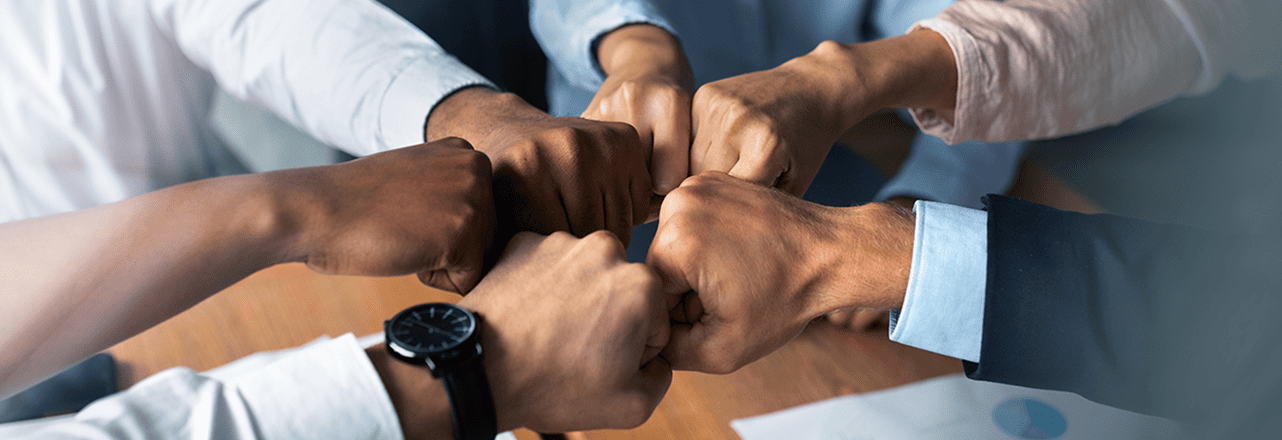 Six people bumping fists in a gesture of unity and teamwork during a business meeting.