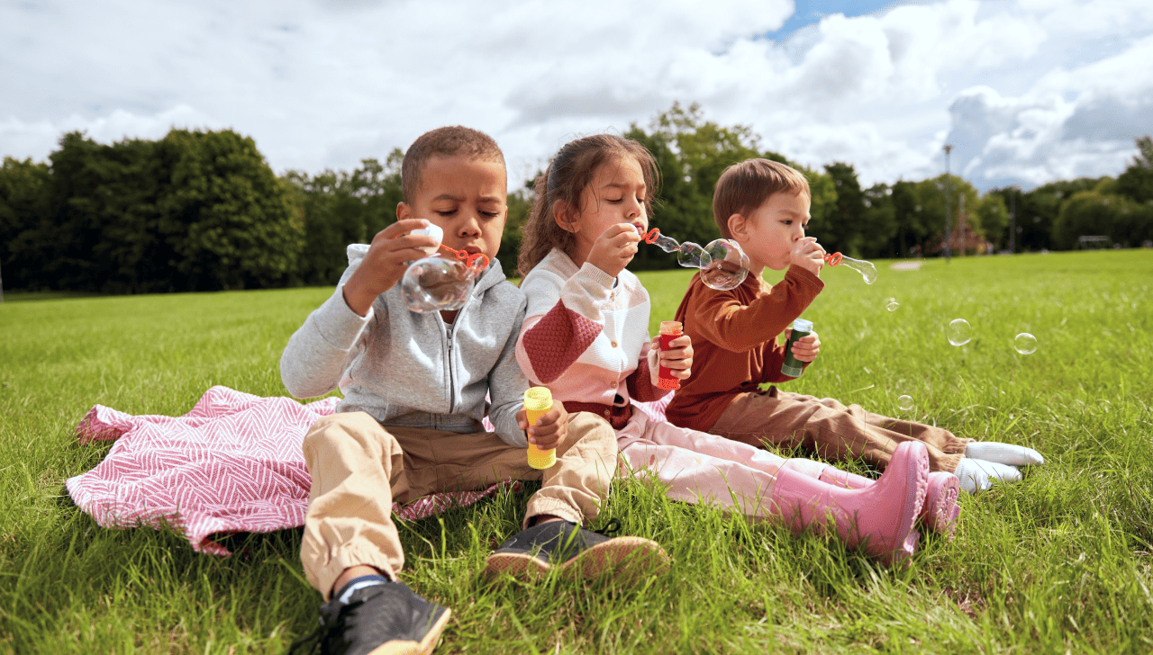 A group of happy children play outside, blowing bubbles.