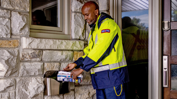 A Canada Post mail carrier places a delivery in a home mailbox.