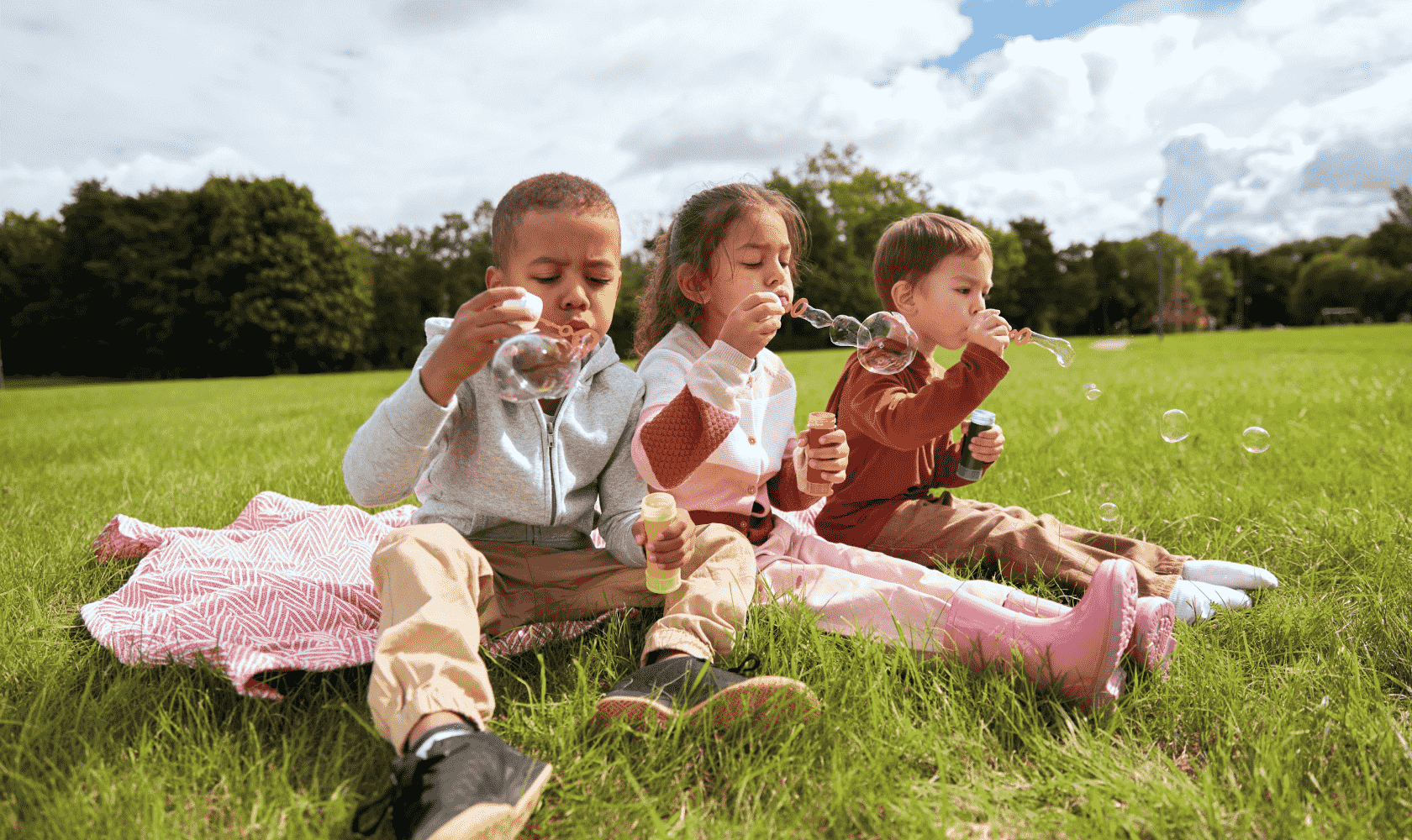 A group of happy children play outside, blowing bubbles.