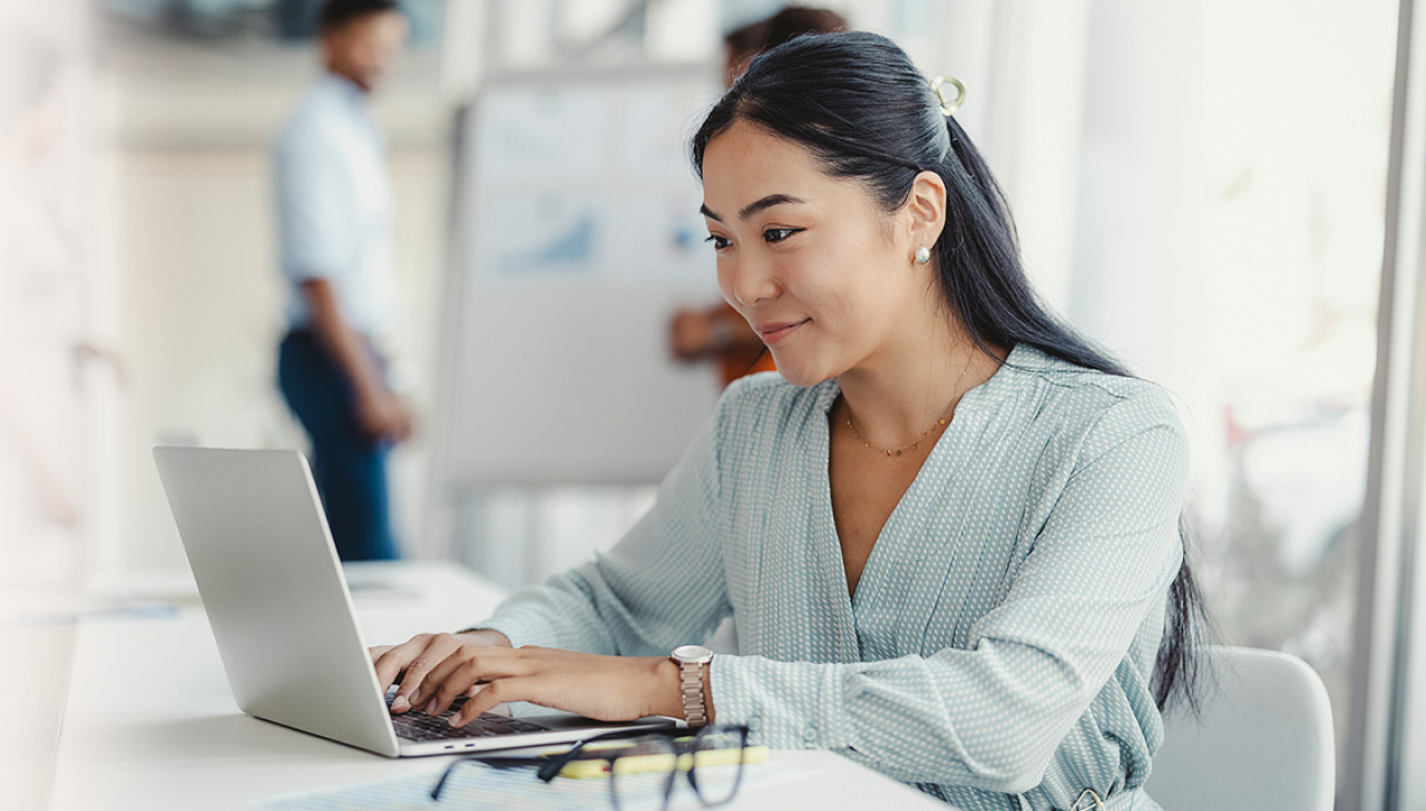 A woman sitting at a worktable uses a laptop.