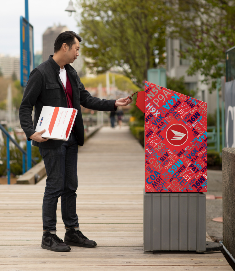A man holding a flat rate box opens a Canada Post street mailbox. A man holding a flat rate box opens a Canada Post street mailbox.