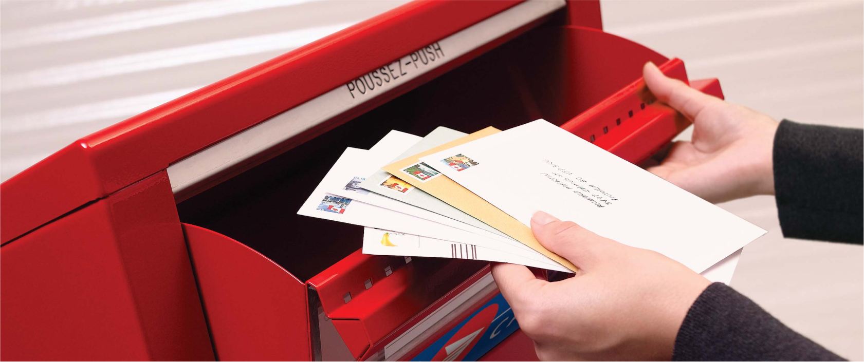 A stack of stamped and addressed envelopes is placed in a Canada Post street letter box to be mailed.