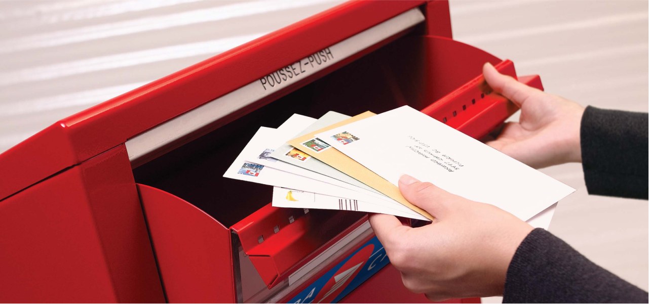 A stack of stamped and addressed envelopes is placed in a Canada Post street letter box to be mailed.