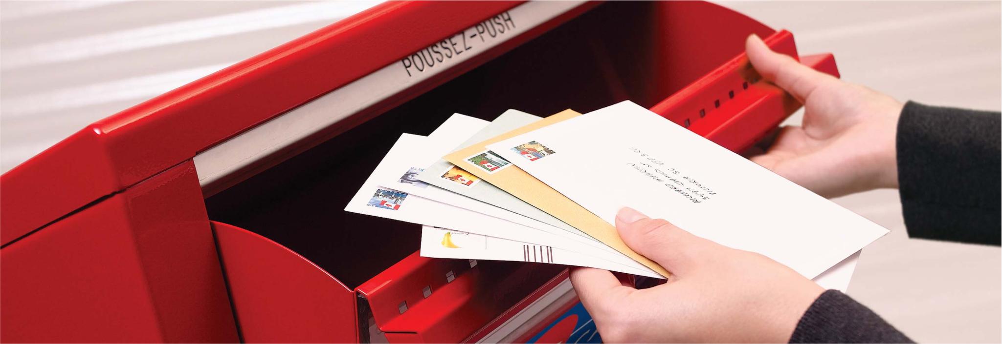 A stack of stamped and addressed envelopes is placed in a Canada Post street letter box to be mailed.