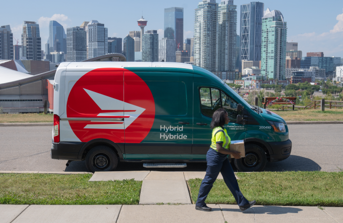 Un nouveau camion de Postes Canada roule sur une rue résidentielle. Il est vert forêt et blanc, avec l’icône du logo rouge et blanc de Postes Canada