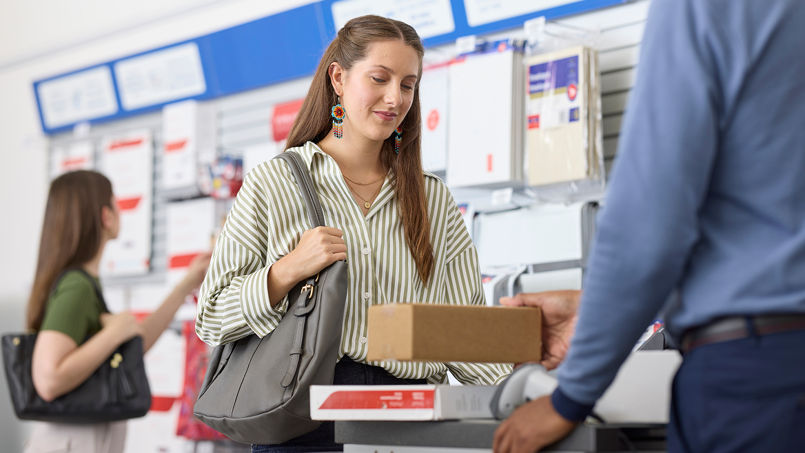 A customer stands at a Canada Post counter while a postal employee scans her packages. 
