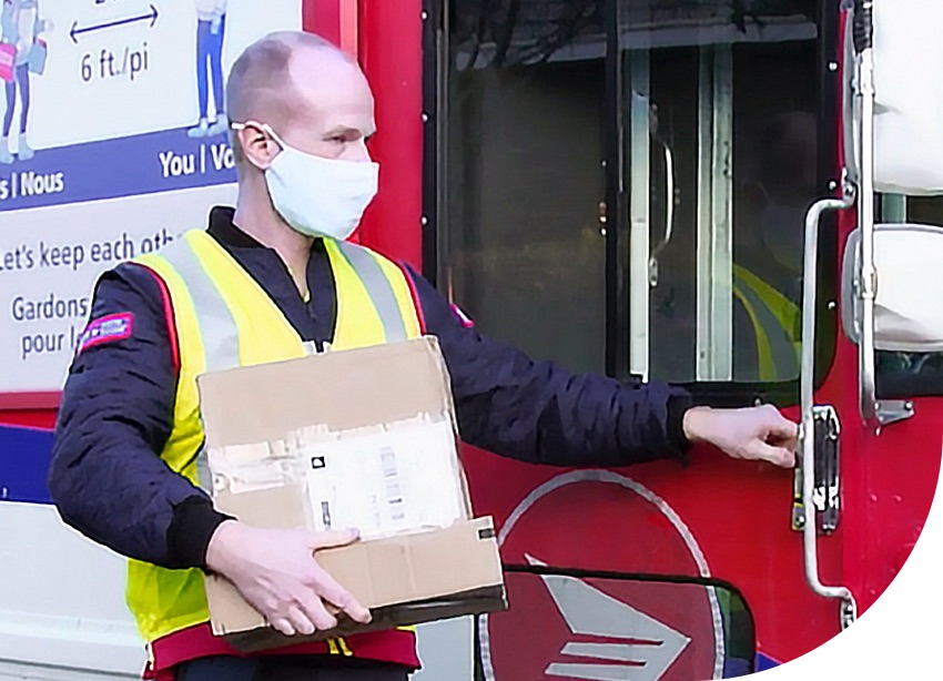 Un agent de livraison de Postes Canada porte un masque et tient un colis près de son véhicule.