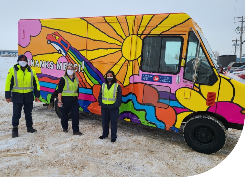 Trois employés de Postes Canada se tiennent près d'un véhicule décoré à l'image du timbre spécial de 2020 pour les employés.