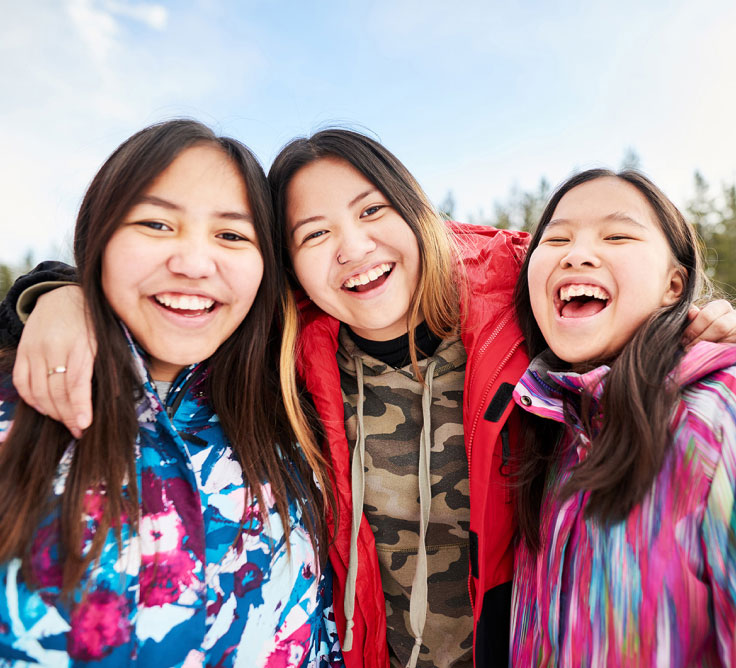Trois étudiantes autochtones sourient et s’enlacent