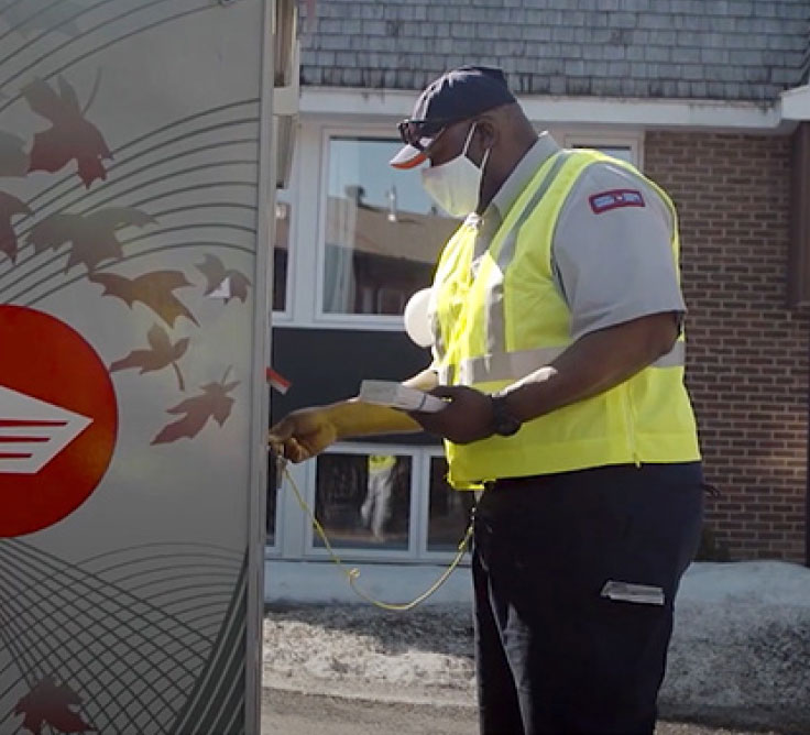 Un employé de Postes Canada porte un gilet de haute visibilité jaune et un couvre-visage. Il déverrouille un véhicule de livraison de Postes Canada.