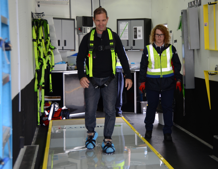 Un employé s’exerce à marcher sur une surface glissante dans un simulateur de glissades à l’intérieur d’une installation de Postes Canada pendant qu’une collègue le regarde