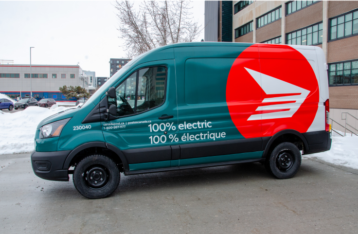 A Canada Post green fleet electric delivery vehicle is parked outside a Canada Post facility. It says 