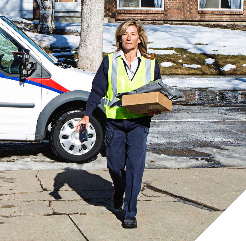 Canada Post employee walks on an icy road carrying multiple parcels.