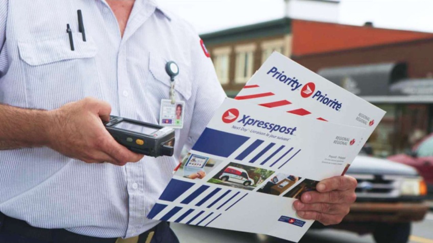 A Canada Post letter carrier scans two Xpresspost prepaid envelopes to update their tracking information.