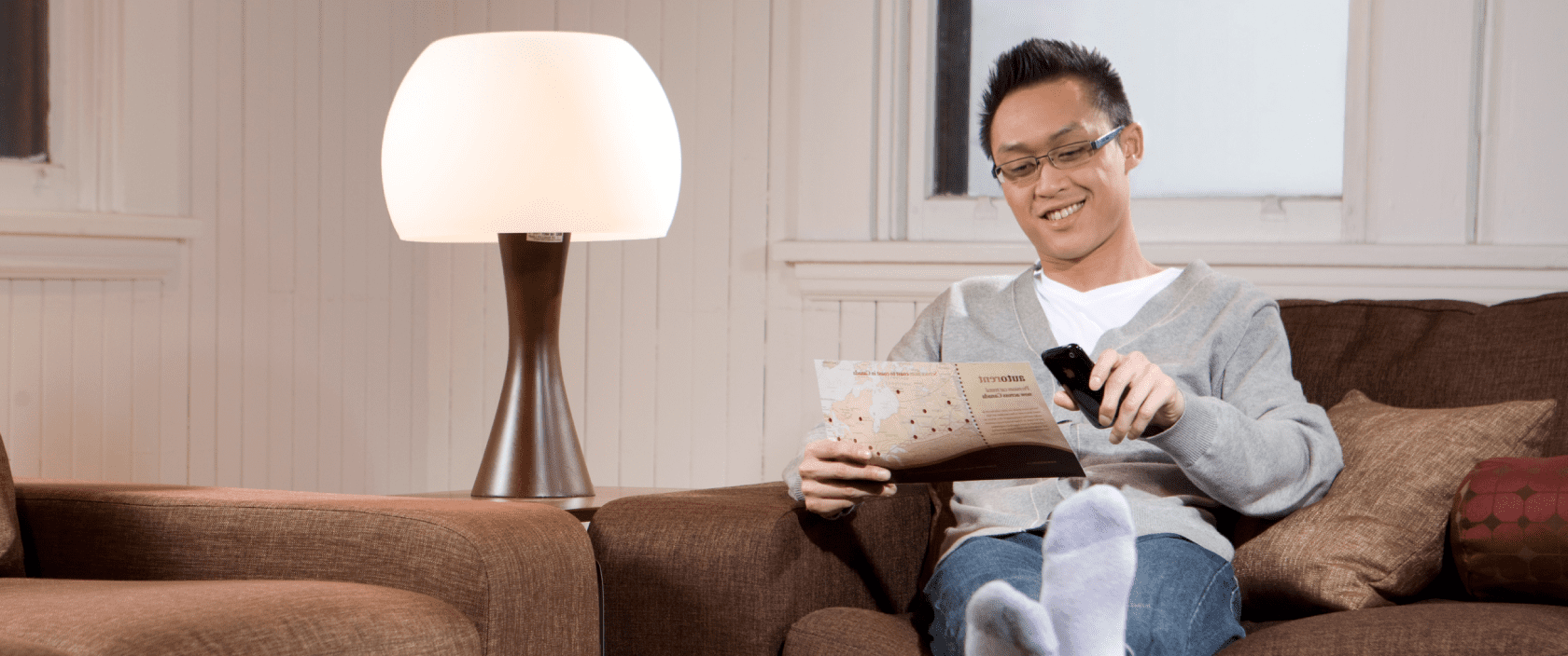 A young man reads a brochure while sitting on a couch in a living room.