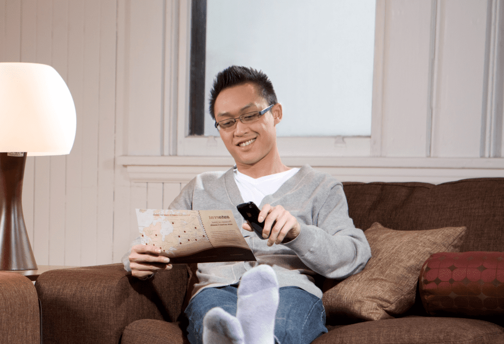 A young man reads a brochure while sitting on a couch in a living room. 
