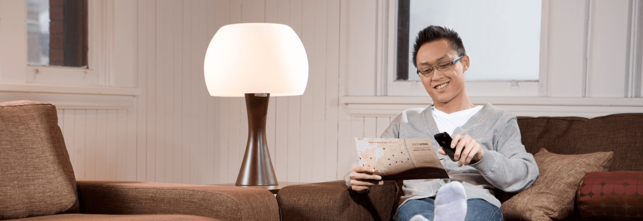 A young man reads a brochure while sitting on a couch in a living room.
