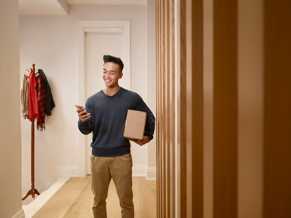 Man in a front hallway holding a package and looking at his mobile phone