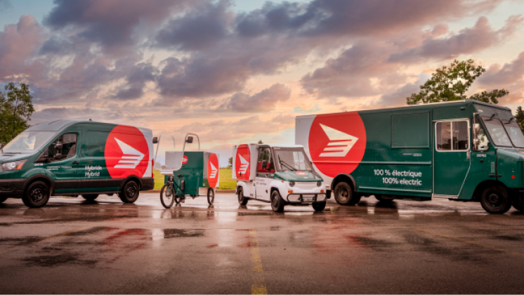 Des véhicules de livraison hybrides et électriques de Postes Canada sont stationnés en rangée.