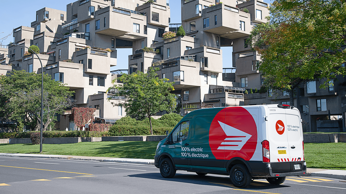A Canada Post green fleet vehicle drives along an urban road near a modern looking condo development.