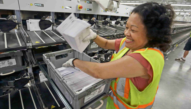 A Canada Post employee sorts mail in a Canada Post facility. She wears a safety vest.