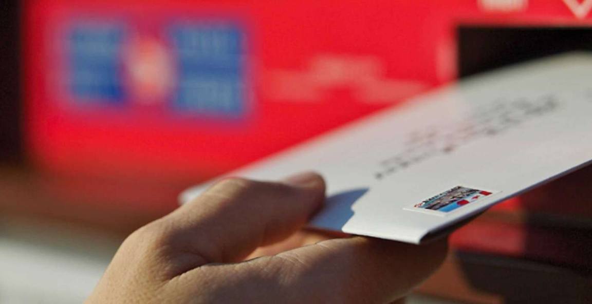 A person deposits an envelope into the slot of a street letter box.