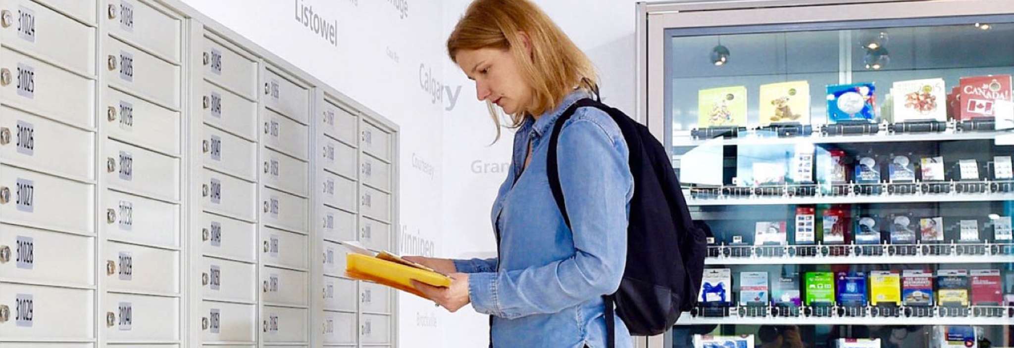 A woman inside a post office sorts through a small stack of mail she has just retrieved from her Canada Post PO box. 