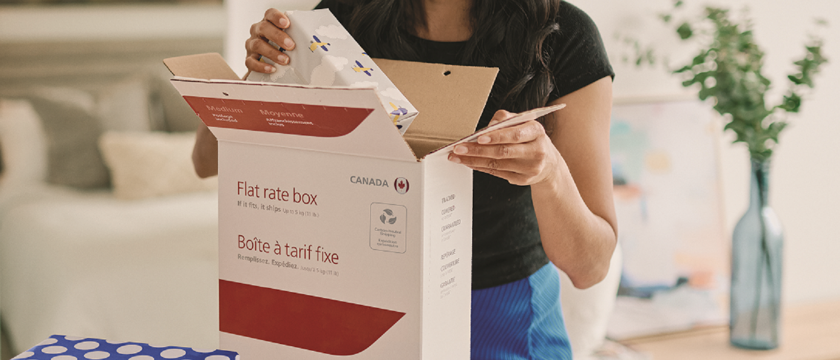 A woman buys a Canada Post flat rate box at a post office counter.