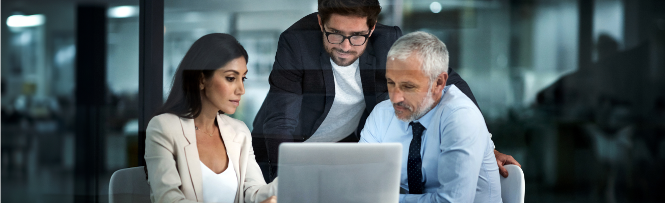 Three co-workers look at a laptop computer screen as they work in a corporate office.