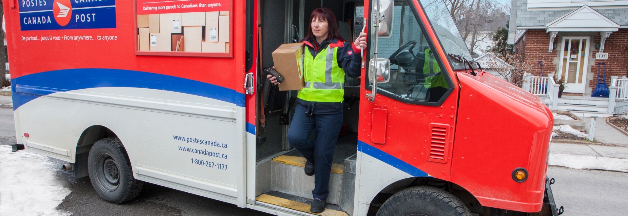 Agente de livraison sortant d’un camion de Postes Canada dans un quartier résidentiel pour livrer un colis