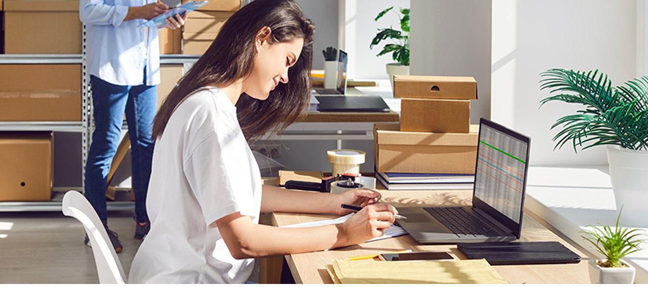 Une femme assise à un bureau écrit sur un bloc de papier devant un ordinateur portable.