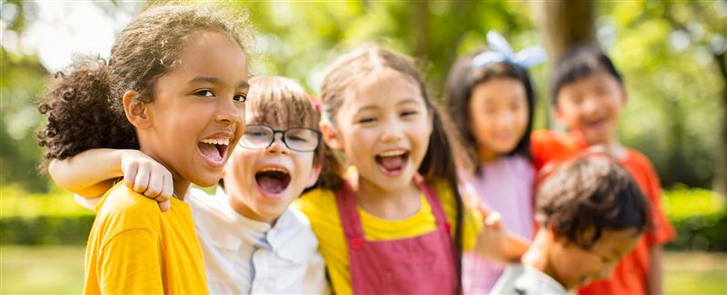 Des enfants souriants sont debout dans une salle de classe, les bras en l’air