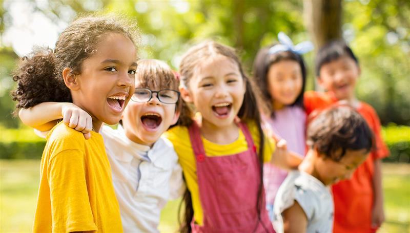 Des enfants souriants sont debout dans une salle de classe, les bras en l’air