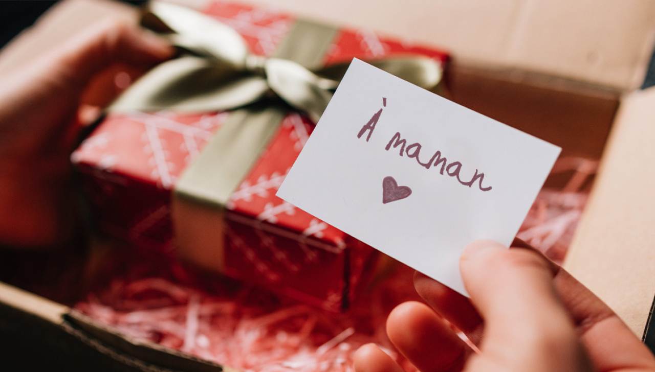 Des mains ouvrent un colis qui contient une boîte-cadeau emballée et une carte sur laquelle il est écrit « À maman »