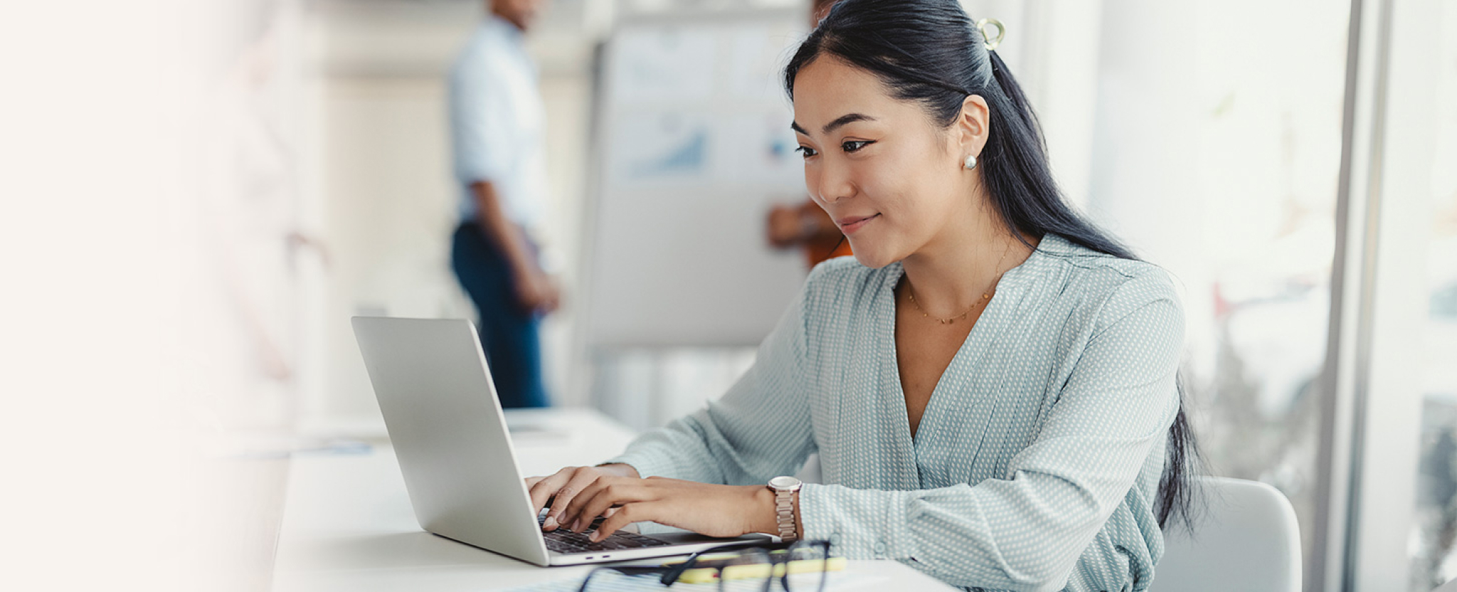 Une femme assise à une table de travail utilise un ordinateur portable