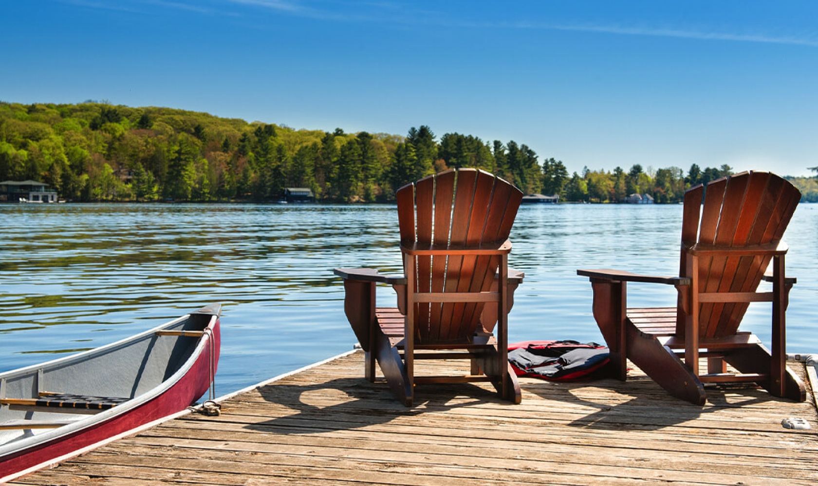 Deux chaises en bois reposent sur un quai au bord d’un lac, à côté d’un canot