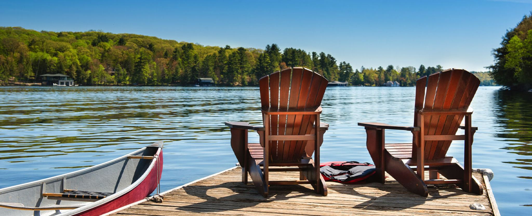 Deux chaises en bois reposent sur un quai au bord d’un lac, à côté d’un canot