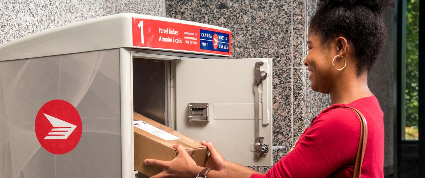 Une femme récupère son colis dans l’casier à colis de Postes Canada dans la salle de courrier de son immeuble d’habitation