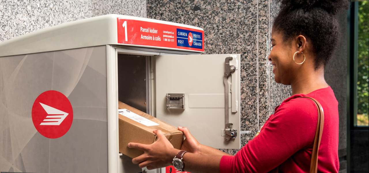 Une femme récupère son colis dans l’casier à colis de Postes Canada dans la salle de courrier de son immeuble d’habitation
