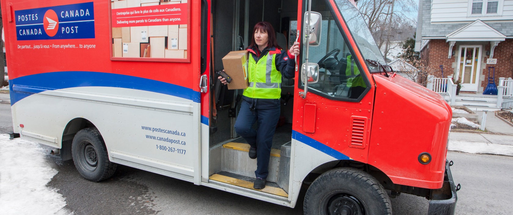 Agente de livraison sortant d’un camion de Postes Canada dansun quartier résidentiel pour livrer un colis