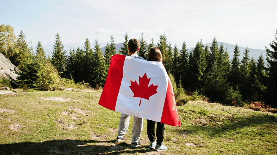 Un homme et une femme enveloppés dans un drapeau canadien admirent une forêt du haut d’une colline. Un homme et une femme enveloppés dans un drapeau canadien admirent une forêt du haut d’une colline.
